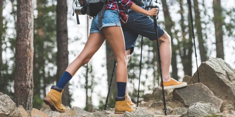 Two hikers navigate a rocky forest trail with trekking poles and sturdy boots.